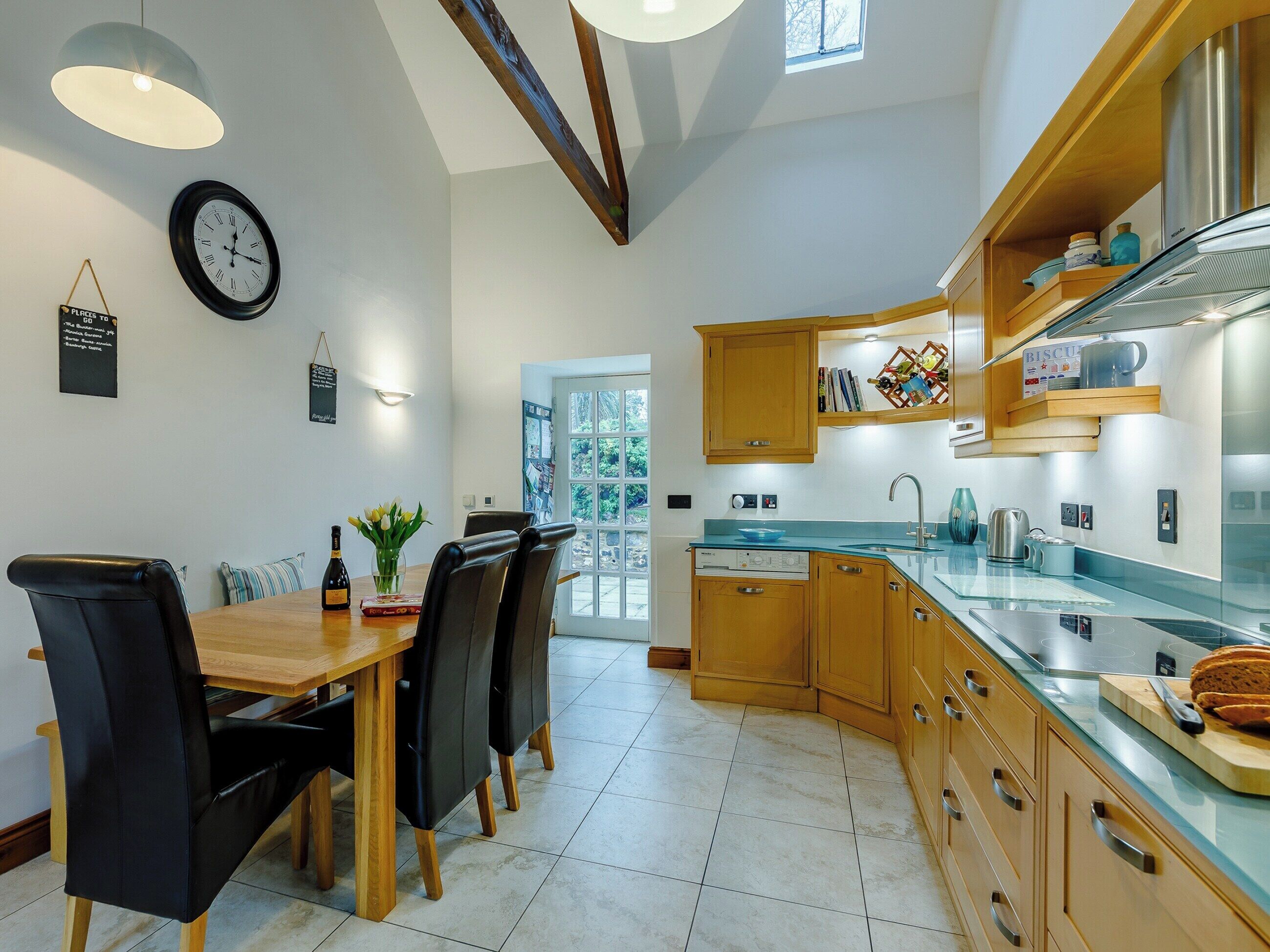 Een moderne keuken met houten kasten, een glazen aanrecht en een eethoek met een houten tafel en stoelen.