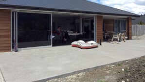 A modern house with a large sliding glass door entrance, a patio with outdoor furniture, and a clear sky. - Glenorchy rise (Glenorchy)