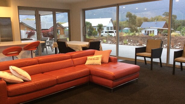 A modern living room with a large sectional sofa, a dining area with a table and chairs, and large windows offering a view of the surrounding landscape. - Glenorchy rise (Glenorchy)