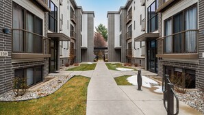 Un moderno edificio de apartamentos con un patio central, que incluye un sendero, pequeños árboles y una zona con nieve.
