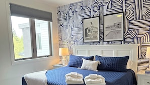 Un dormitorio con cama, ventilador de techo, ventana, pared con diseño y un cuadro enmarcado.