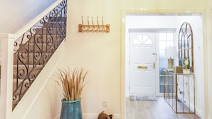 A wooden staircase with a decorative railing, a blue vase with tall plants, a small dog, a white door, and a console table with a lamp and decorative items.