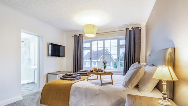A hotel room with a bed, bedside table, lamp, window, and a TV on the wall.
