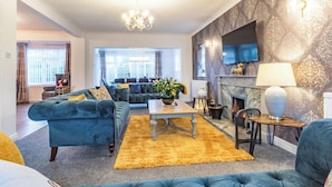 A living room with a blue sofa set, a yellow rug, a fireplace, and a chandelier.
