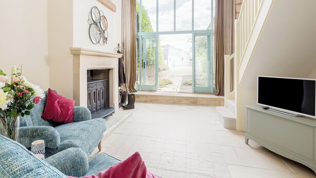 A living room with a fireplace, a television, and a large window with curtains. - 1 bedroom accommodation in Old Sodbury, near Bristol (Old Sodbury, near Bristol)