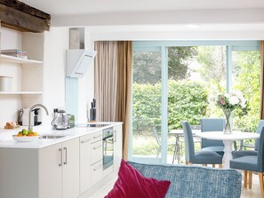 Une cuisine moderne dotée d’un four encastré, un coin repas avec une table et des chaises, et une grande fenêtre offrant une vue sur la verdure.