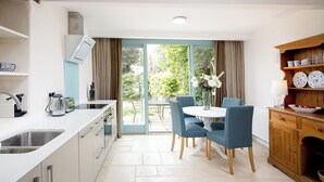 A modern kitchen with a dining area, a view to the outside, and a wooden cabinet with dishes. - 1 bedroom accommodation in Old Sodbury, near Bristol (Old Sodbury, near Bristol)