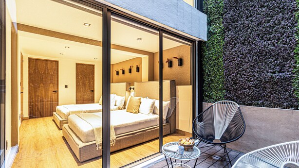 A modern hotel room with a large bed, a separate seating area with a table and chairs, and a view of a green wall outside. - Casa Horacio by Kukun (Mexico City)