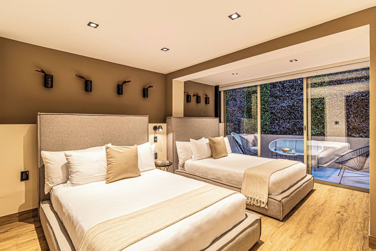 A modern hotel room with two beds, a balcony with a view, and a large window.