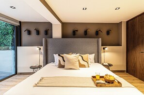 Habitación de hotel moderna con una cama grande, mesitas de noche, una bandeja con desayuno y vistas a zonas verdes.