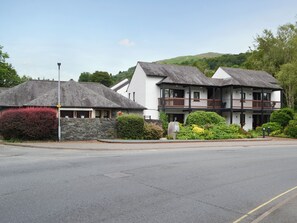 A two-story building with a balcony on the upper floor, a stone wall, and a red bush in the foreground.