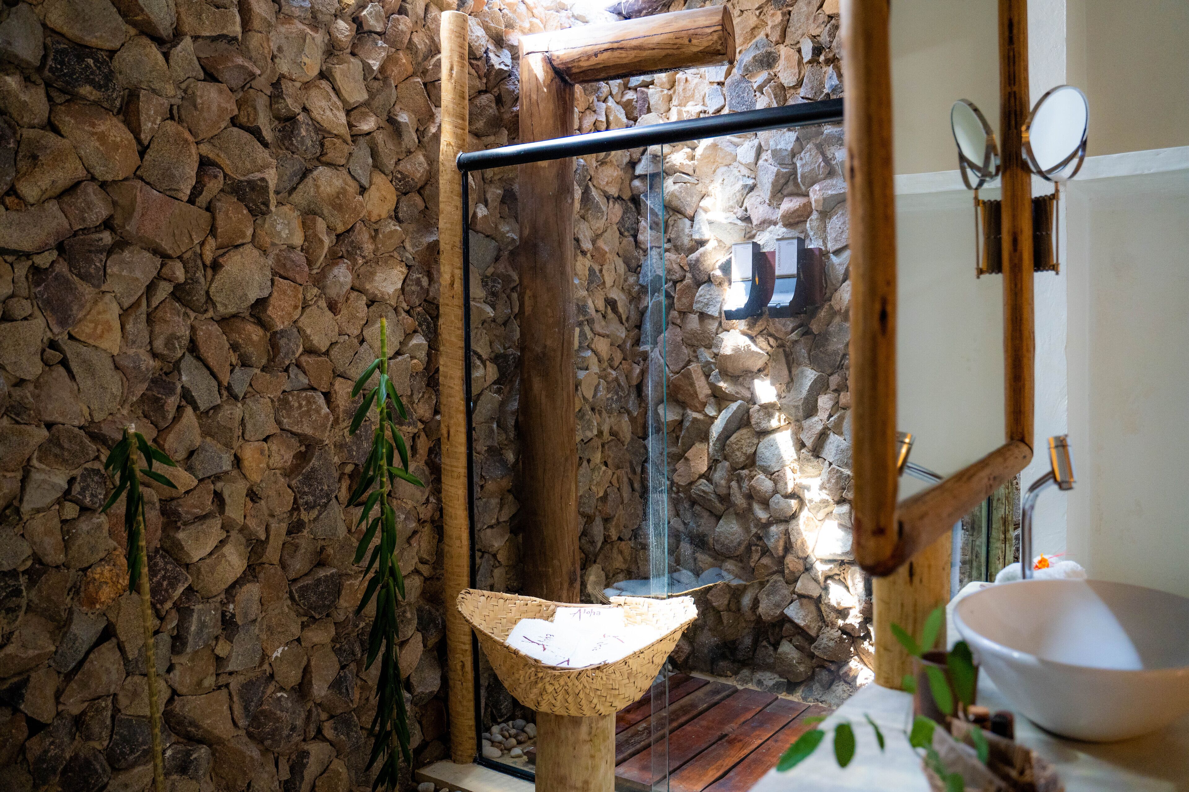 Une salle de bain aux murs en pierre, avec un lavabo en bois et une cabine de douche en verre.