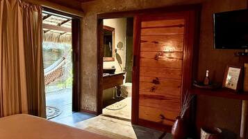 Un dormitorio con una cama grande, una puerta de madera, un televisor y una mesita con una botella y un objeto enmarcado.