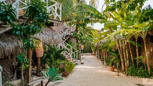 A tropical resort with a thatched-roof building, a wooden staircase, and a sandy pathway lined with plants. - Aloha Village Hotel (Amontada)