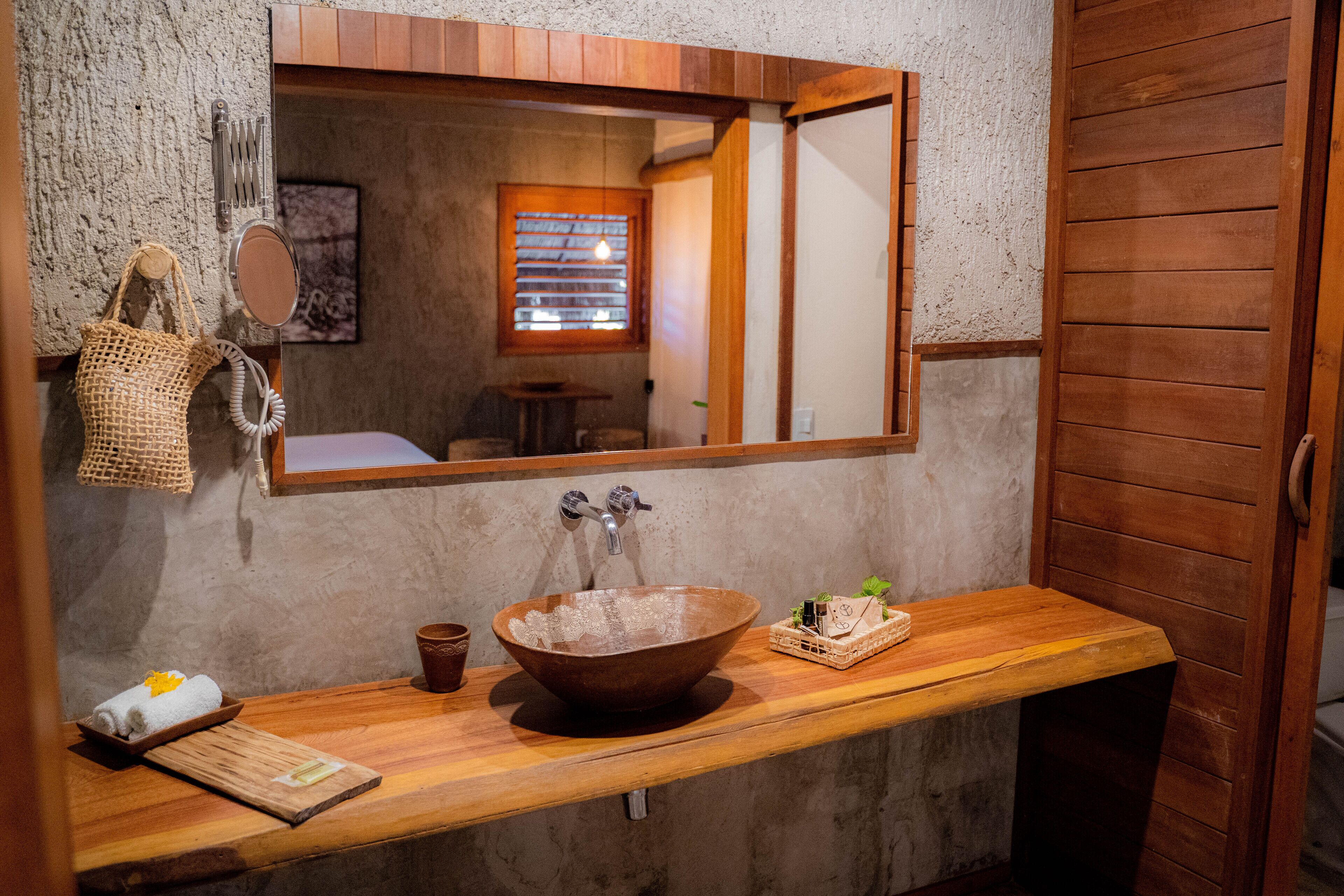 Ein Badezimmer mit einem Holzbadezimmer-Möbel, einem großen Spiegel, einem Waschschalenbecken und einem kleinen Holztisch mit Toilettenartikeln.