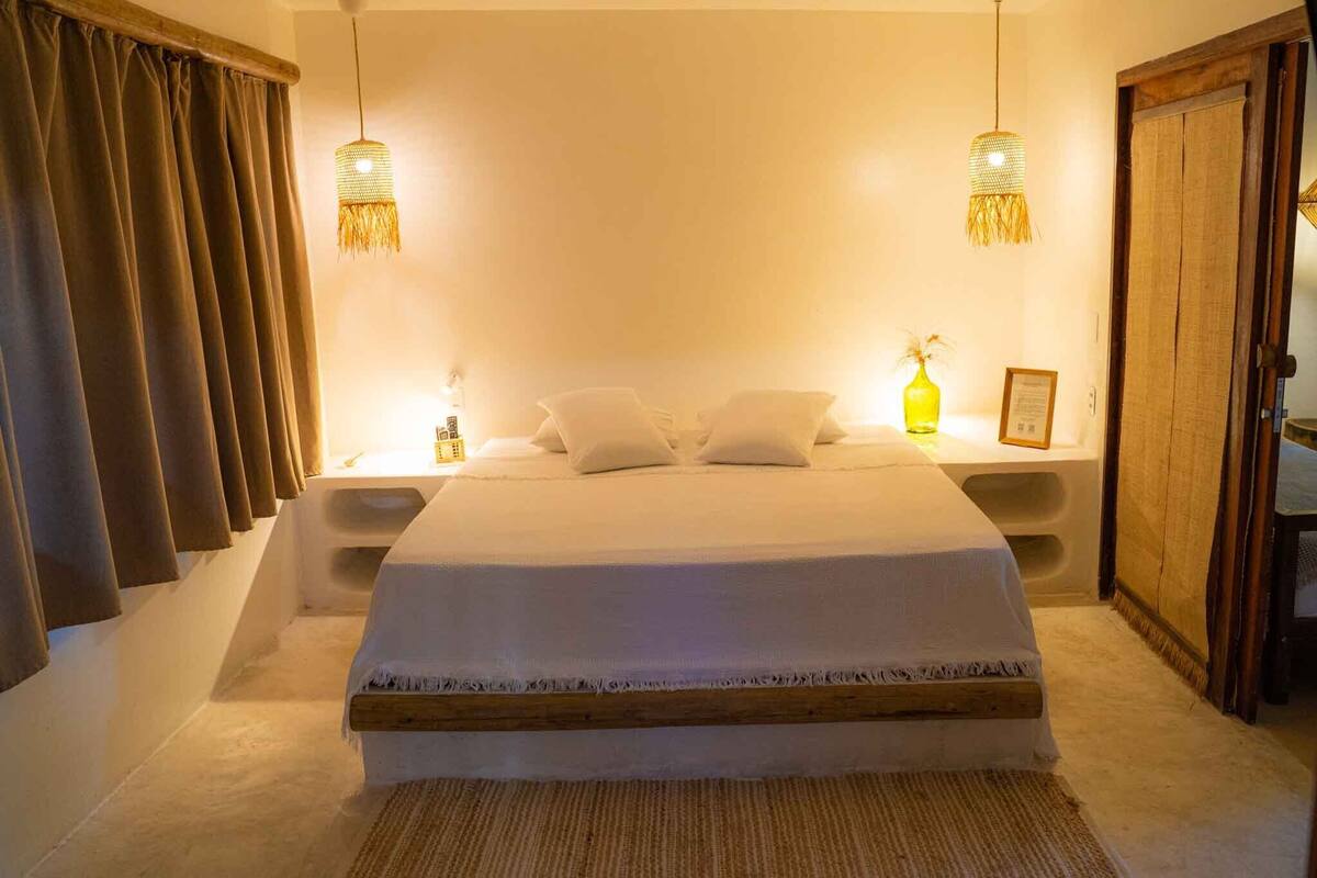 A bedroom with a large bed, two bedside tables, a wooden wardrobe, and a hanging light fixture.