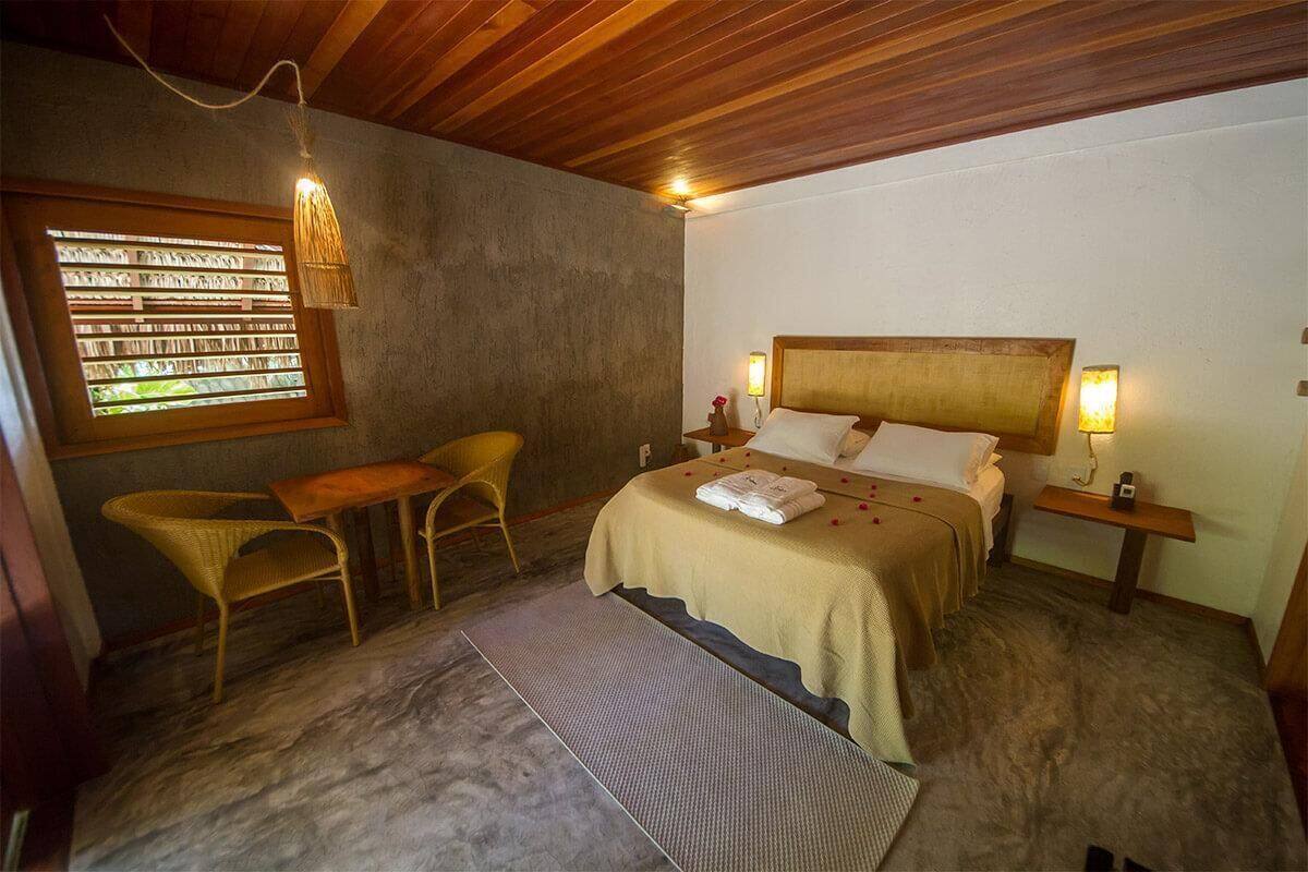 A bedroom with a bed, bedside tables, a small table, two chairs, a window with blinds, and a hanging light fixture.