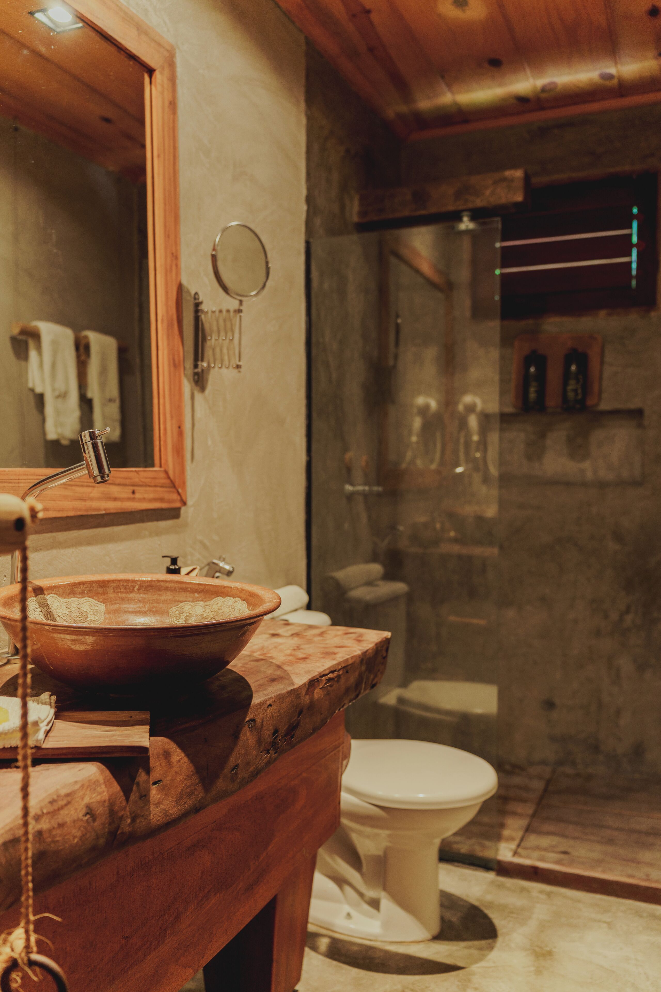 A rustic bathroom with a wooden basin, a mirror, a toilet, and a shower area.