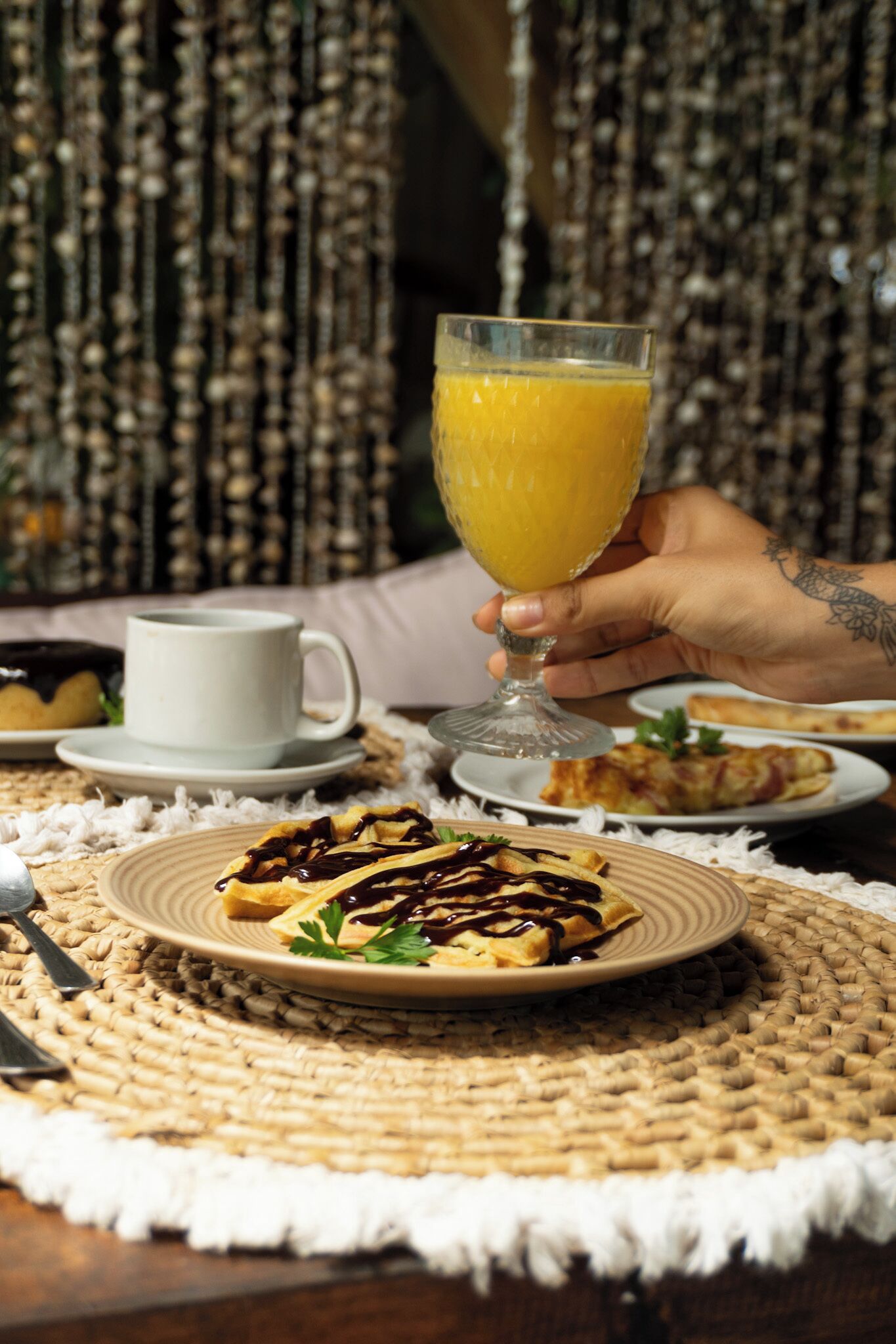 A breakfast setting with a glass of orange juice, a plate of pancakes with chocolate sauce, and a cup of coffee on a woven placemat.