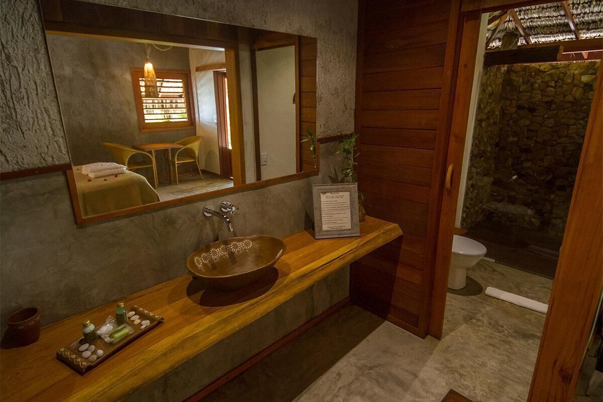 Un baño con tocador de madera, un espejo grande, pared de piedra y una ventana pequeña.
