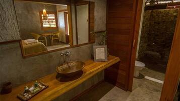 Un baño con tocador de madera, un espejo grande, pared de piedra y una ventana pequeña.