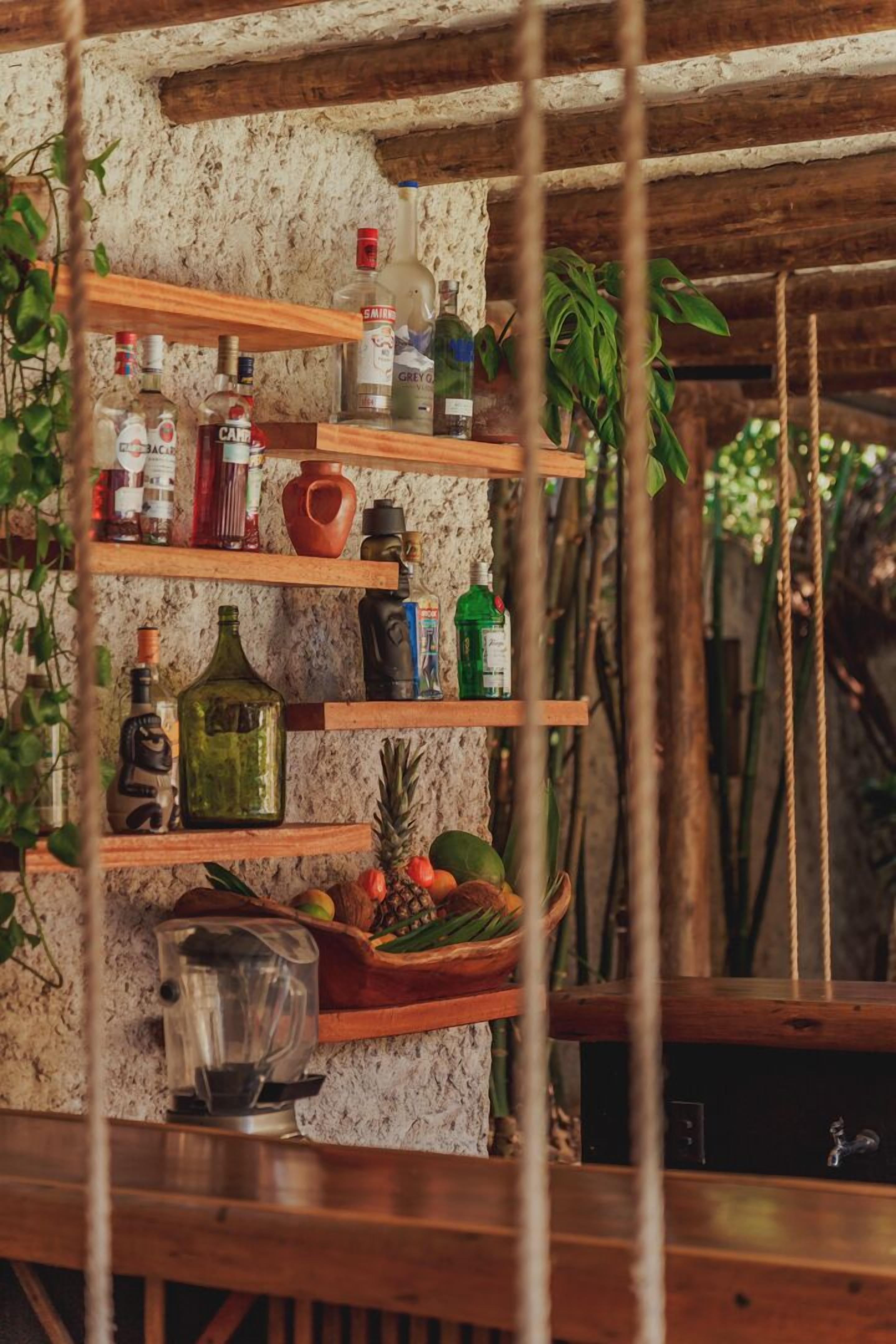 A rustic bar area with wooden shelves holding various bottles and a fruit basket.