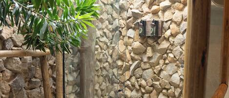 A glass-enclosed shower area with a stone wall, wooden ladder, and a potted plant.