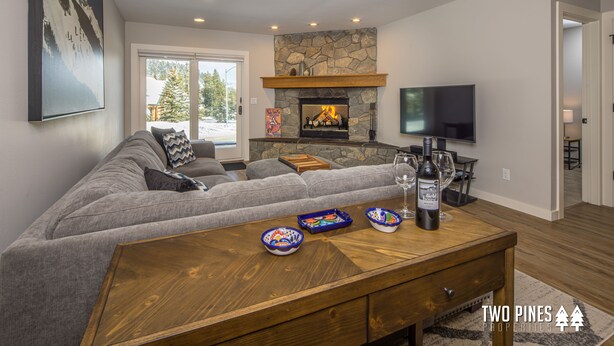 A modern living room with a stone fireplace, a large flat-screen TV, and a cozy seating area. - New Charming Big Horn Ski-In/Out Home! Cozy Fireplace, Walk to Resort! (Big Sky)