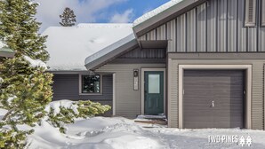 A two-story house with a snow-covered roof and a garage door. - New Charming Big Horn Ski-In/Out Home! Cozy Fireplace, Walk to Resort! (Big Sky)