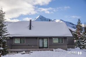 Ein modernes, zweistöckiges Haus mit schneebedecktem Dach, großen Fenstern und einem Schornstein.