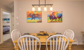 Un comedor con una mesa de madera, sillas blancas y dos cuadros coloridos de bisontes en la pared.
