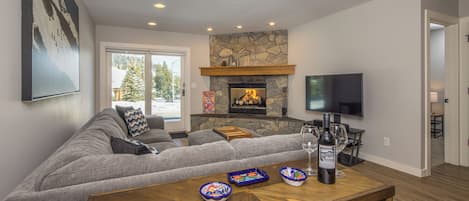 Una sala de estar moderna con una chimenea de piedra, un televisor de pantalla plana grande y una zona de estar acogedora.
