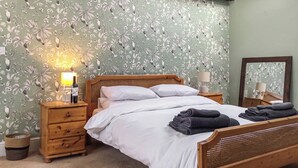 A bedroom with a floral wallpaper, a wooden bed, two bedside tables with lamps, and a mirror on the wall. - 2 bedroom accommodation in Longhorsley, Near Morpeth (Longhorsley, Near Morpeth)