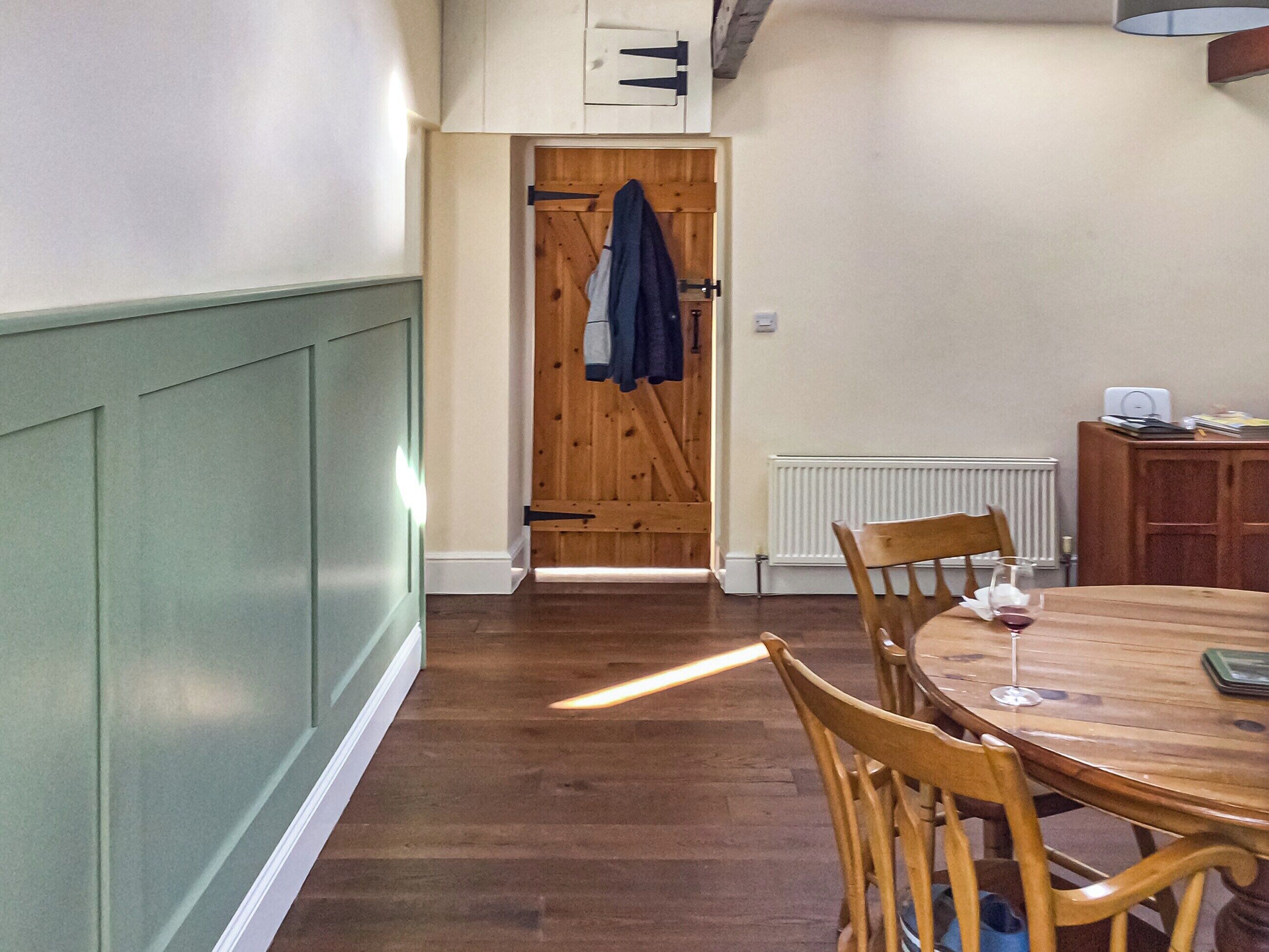 A dining area with a wooden table and chairs, a radiator, and a wooden door with a coat hanging on it.