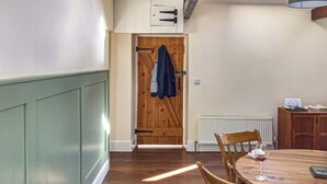 A dining area with a wooden table and chairs, a radiator, and a wooden door with a coat hanging on it. - 2 bedroom accommodation in Longhorsley, Near Morpeth (Longhorsley, Near Morpeth)
