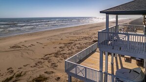 Vista a la playa con terraza de madera y mobiliario exterior.