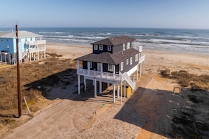 A two-story beach house with a balcony, a sandy beach in the background, and the ocean. - Deck & Ocean Views: Beachfront Home in Freeport (Freeport)