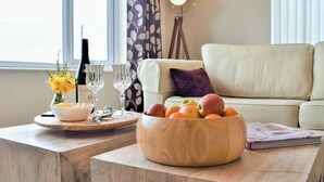 A living room with a sofa, a wooden table with a bowl of fruit, a wine bottle, and glasses. - 3 bedroom accommodation in Beadnell (Beadnell)