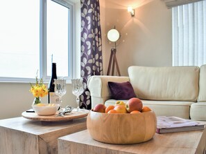 Ein Wohnzimmer mit einer Couch, einem Holztisch mit einer Obstschale, einer Weinflasche und Gläsern.