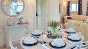 A dining area with a round table set for four, white chairs, a vase with pink flowers, and a mirror above the table. - 3 bedroom accommodation in Beadnell (Beadnell)