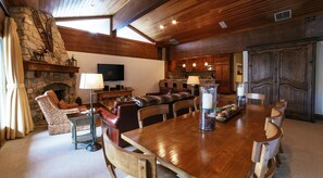 Ein großzügiges Wohnzimmer mit Kamin aus Stein, Holzboden und einem großen Esstisch mit Stühlen.