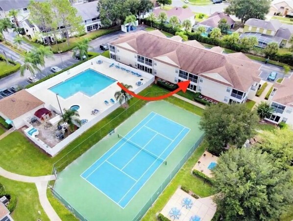 Vue aérienne d’un quartier résidentiel avec une grande piscine et un court de tennis.