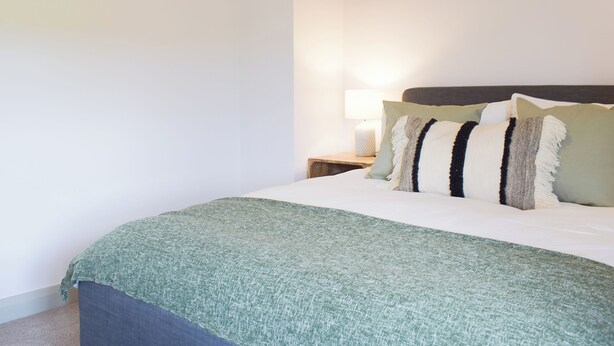 A bedroom with a bed, pillows, a nightstand with a lamp, and a wooden beam above the bed. - 3 bedroom accommodation in Whitchurch (Whitchurch)