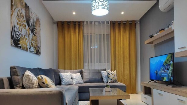 Een moderne woonkamer met een bank, salontafel, televisie en gordijnen.