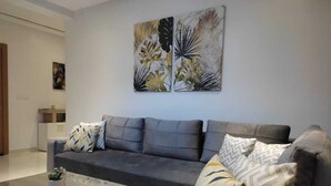 Een moderne woonkamer met een grijze bank, een houten salontafel en decoratieve kussens.
