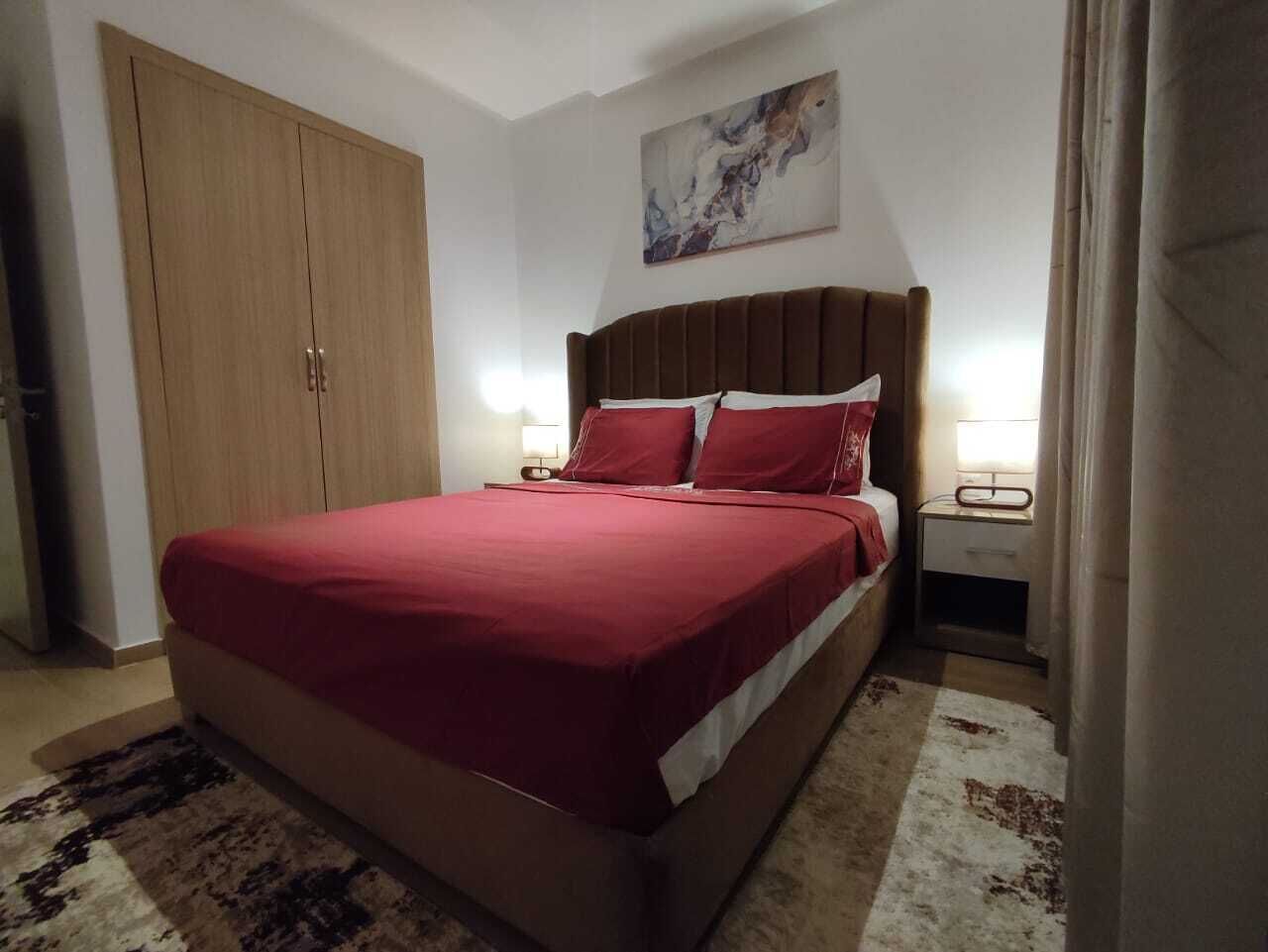 A bedroom with a bed, nightstands, a wardrobe, and a painting on the wall.