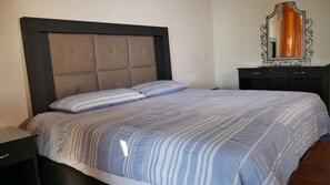 A neatly made bed with a striped bedspread and two pillows, a dark headboard, a small bedside table, and a dresser with a mirror.