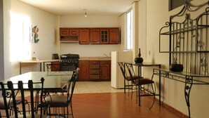 A kitchen with wooden cabinets, a stove, and a dining area with a glass table and metal chairs. - Casa Rinconsito Miramar (Santa Cruz)
