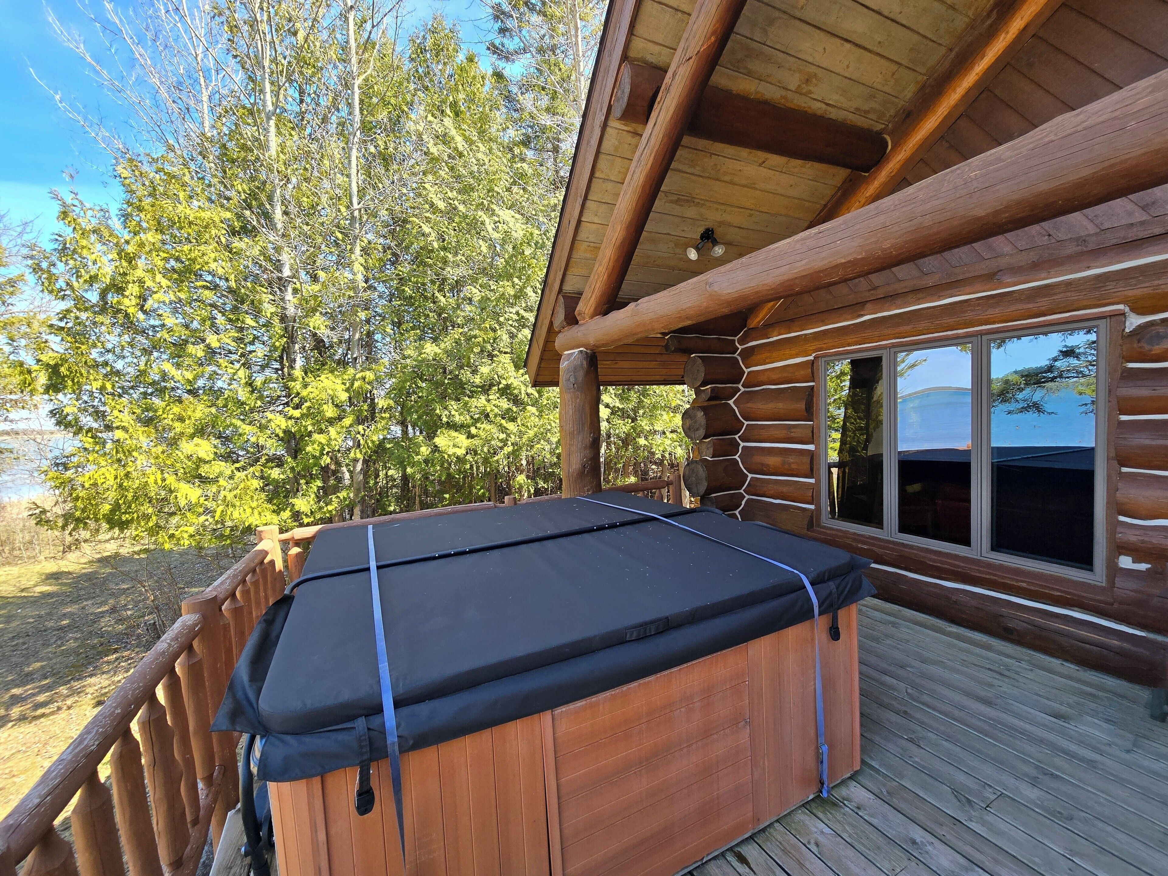 Una cabaña de madera con un jacuzzi en una terraza, rodeada de árboles y un lago.