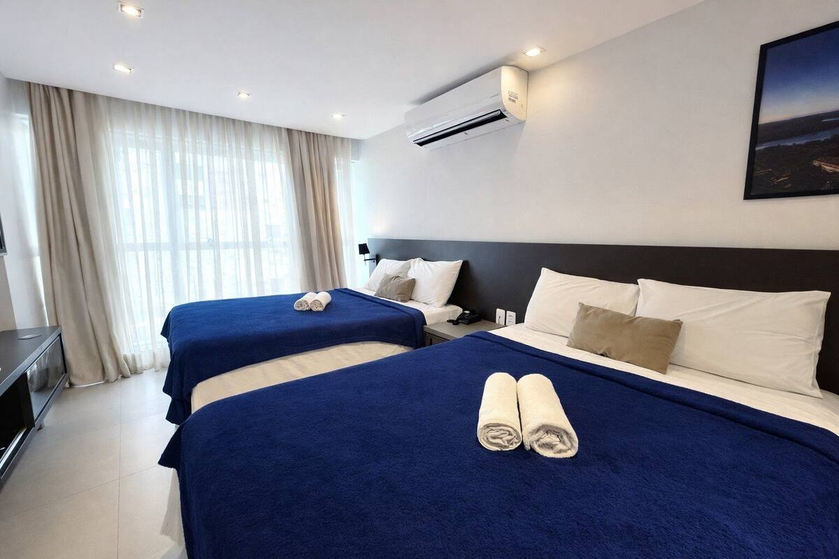 A hotel room with two beds, a TV, and an air conditioning unit.